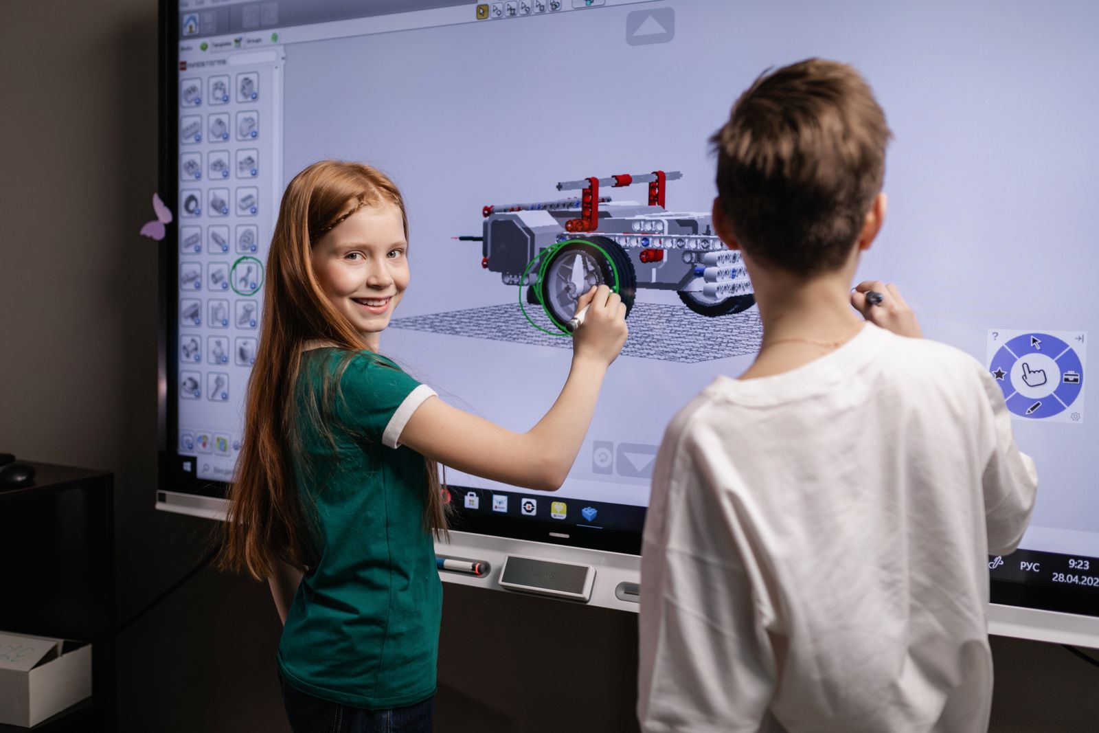 Dos niños trabajan juntos en un modelo 3D sobre una pantalla grande